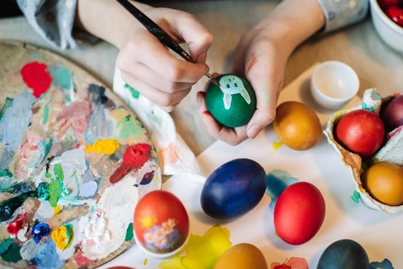 Eine Person bemalt mit einem Pinsel ein grünes Osterei.